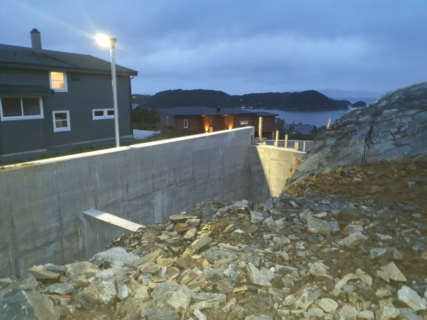 Grunnmur og forskaling sprengt ned i bratt fjelltomt med sjøutsikt i skumring